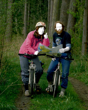 Zwei Fahrradfahrer orientieren sich in einem Wald mit Landkarte