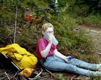 Mdchen sitzt in einem Waldstck und trinkt aus ihrer Feldflasche